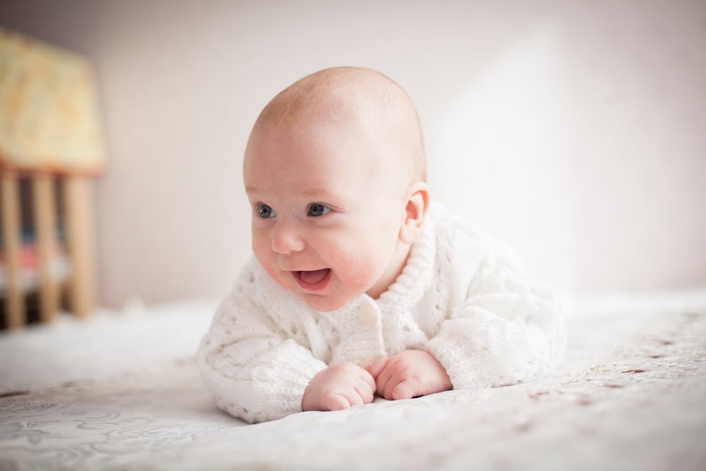 A cute baby smiling on a soft, patterned blanket indoors. Bright and heartwarming moment. newborn sleep tips without sleep training