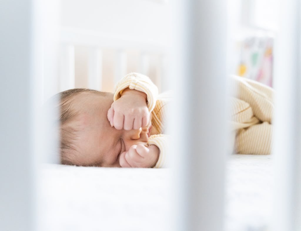 A serene sleeping baby rests peacefully in a bright and cozy crib, framed by white bars. newborn sleep tips without sleep training